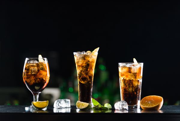 Three glasses of iced beverages in front of a black background